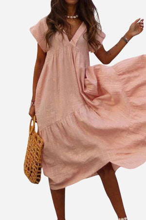 Woman wearing pink V neck tiered cotton midi dress with short sleeves and frill hem holding woven bag