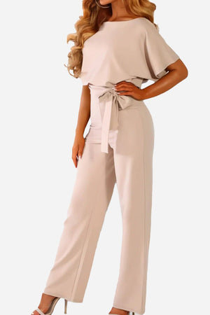 Woman wearing chic short-sleeved wide-leg jumpsuit with belt in light beige color