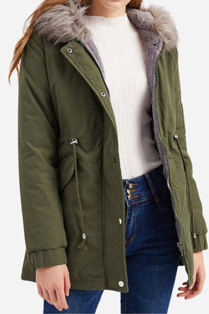 Women wearing olive green fur collar fleece coat with hood and adjustable drawstrings over white sweater and blue jeans
