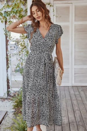 Woman wearing Elegant Blossoms Boho Maxi Dress with floral pattern and belted ruffle hem on porch background