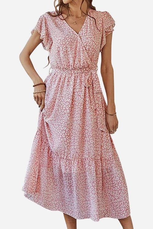 Woman wearing an Elegant Blossoms Boho Maxi Dress in soft pink floral wrap design with V-neck and belted ruffle hem