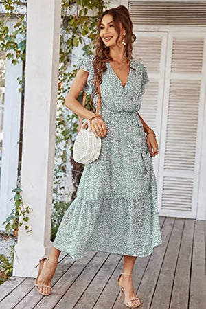 Woman wearing Elegant Blossoms Boho Maxi Dress with floral print, V-neck, short sleeves, ruffled hem, and belt, accessorized with a white round handbag and nude heels.