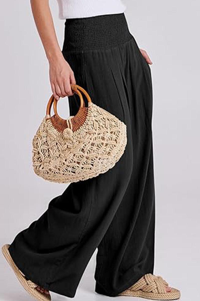 Black palazzo pants with a high smocked waist worn with a white top and woven handbag in hand