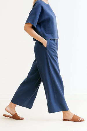 Woman wearing navy blue loose fit co-ord set with wide-leg pants and short sleeve top paired with brown slide sandals