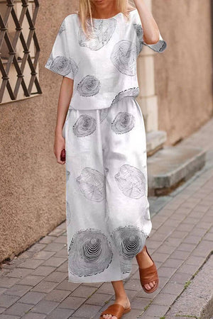 Woman wearing white loose fit co-ord set with abstract circular prints and wide-leg pants walking on a sidewalk