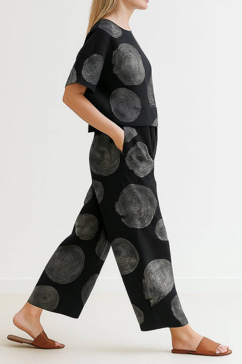 Woman wearing black loose fit co-ord set with large gray circular patterns, wide-leg pants, and relaxed short-sleeve top