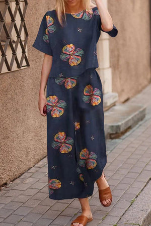 woman wearing navy blue loose fit co-ord set with colorful floral prints and brown sandals walking on sidewalk