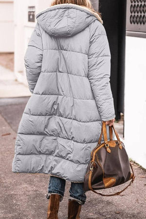 Back view of a woman wearing a gray Sherpa-lined hooded teddy coat carrying a brown handbag outdoors