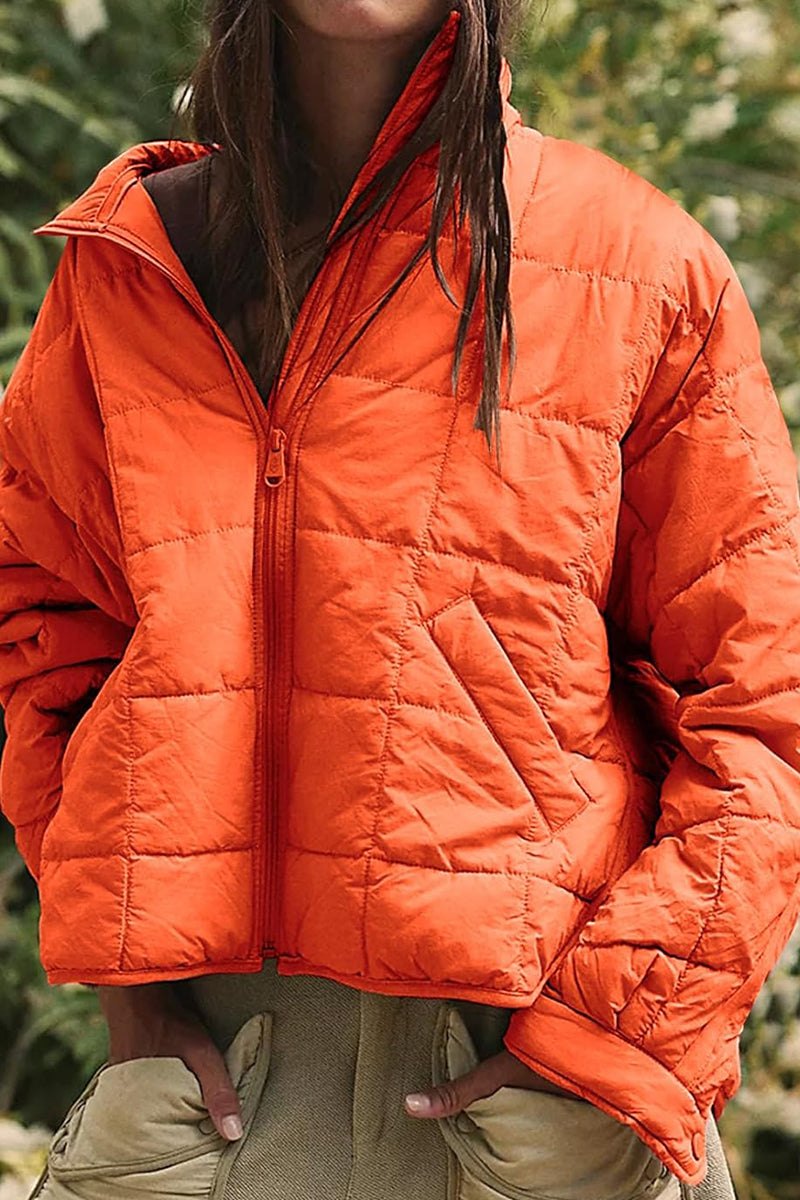 Orange lightweight puffer travel jacket with zip front and pockets, ideal for stylish and compact travel warmth.