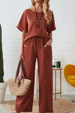 Woman wearing a rust-colored rolled cuff top and patch pocket pants set with relaxed fit, styled with a straw handbag and necklace in a cozy indoor setting
