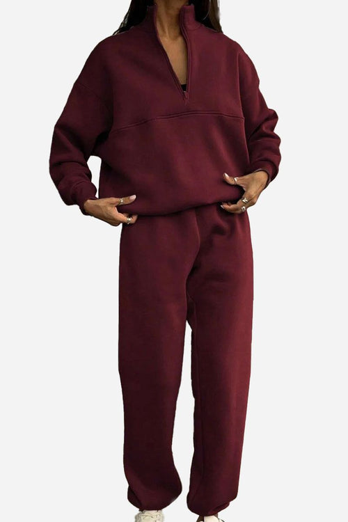Woman wearing a burgundy cotton-blended two-piece tracksuit with high collar and deep zipper.