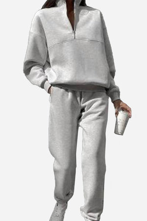 Woman wearing grey cotton-blended two-piece tracksuit with high collar and zipper, holding a cup