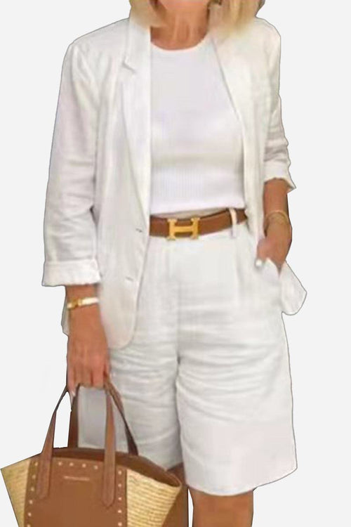 Woman wearing white blazer and high-waisted shorts with a brown belt and carrying a brown handbag