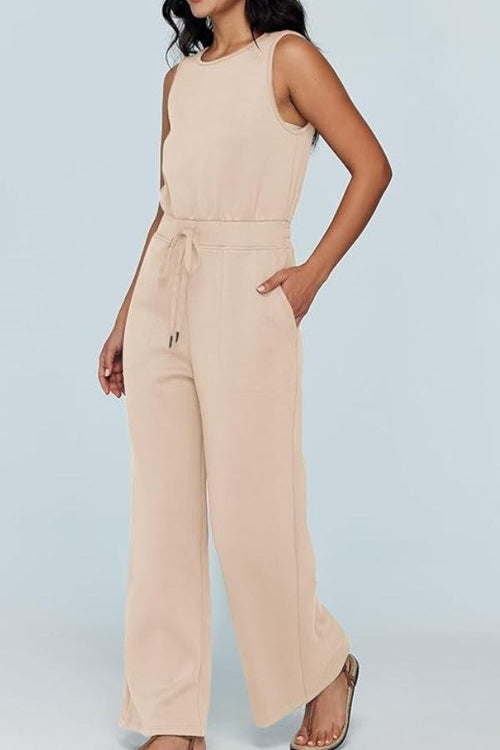 Woman wearing beige sleeveless wide leg pants jumpsuit with drawstring waist and pockets