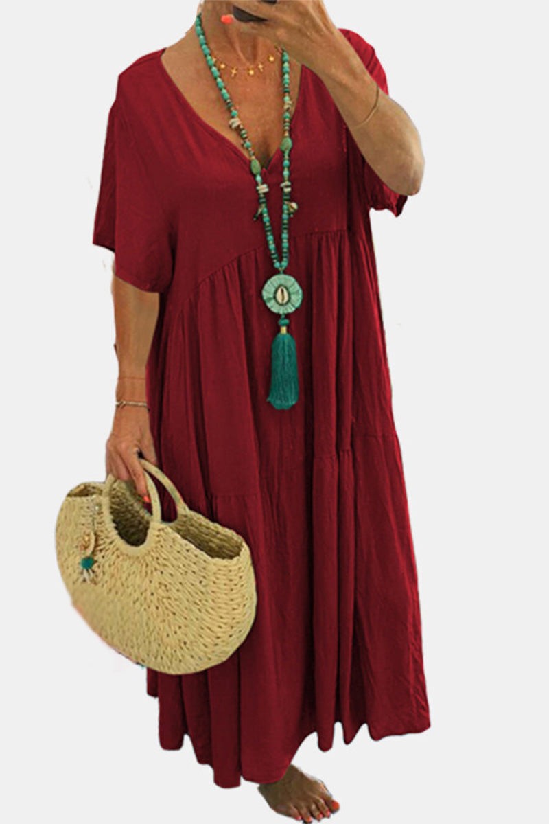 Woman wearing red V-neck two-tiered maxi swing dress holding straw handbag and turquoise necklace