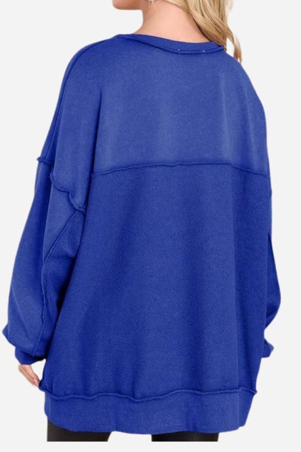 Back view of a woman wearing a blue oversized urban sweatshirt with slouchy sleeves and raw seam detailing.