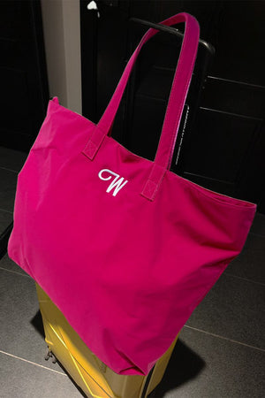 Bright pink waterproof travel bag with sturdy handles resting on yellow suitcase handle