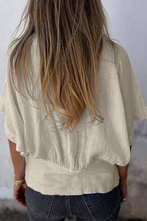Back view of a woman wearing a beige 100% pure linen short-sleeve blouse with a relaxed fit and natural wrinkles.