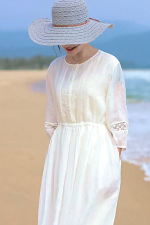 woman wearing white 100% linen coastal shift dress with lace sleeves and wide brim hat on beach