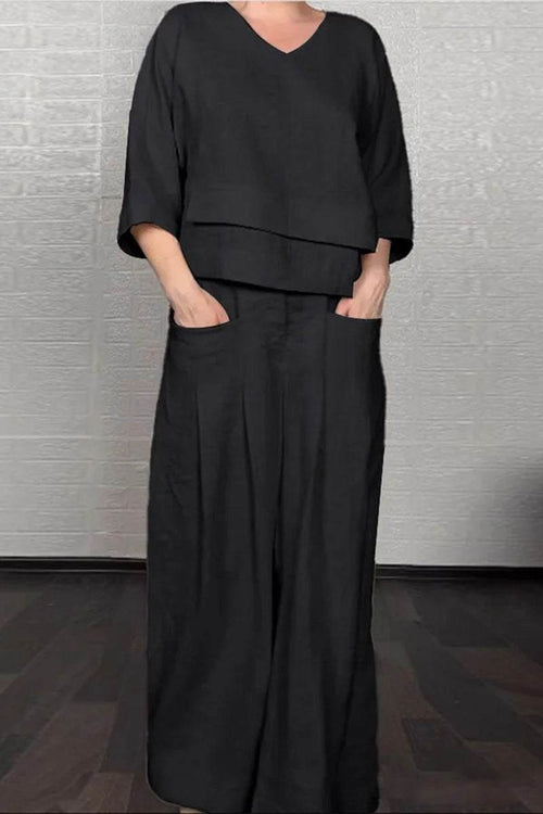 Woman wearing black Atelier Serenity Layered Two-Piece Set with V-neck layered top and wide-leg trousers standing indoors