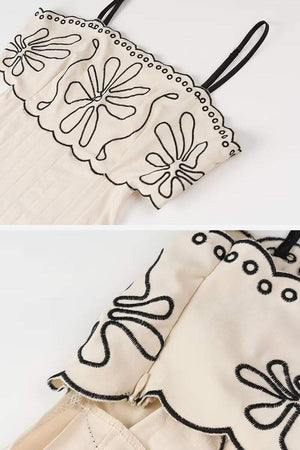 Close-up of artisan embroidered scalloped edge cream dress bodice with black floral stitch detailing and spaghetti straps