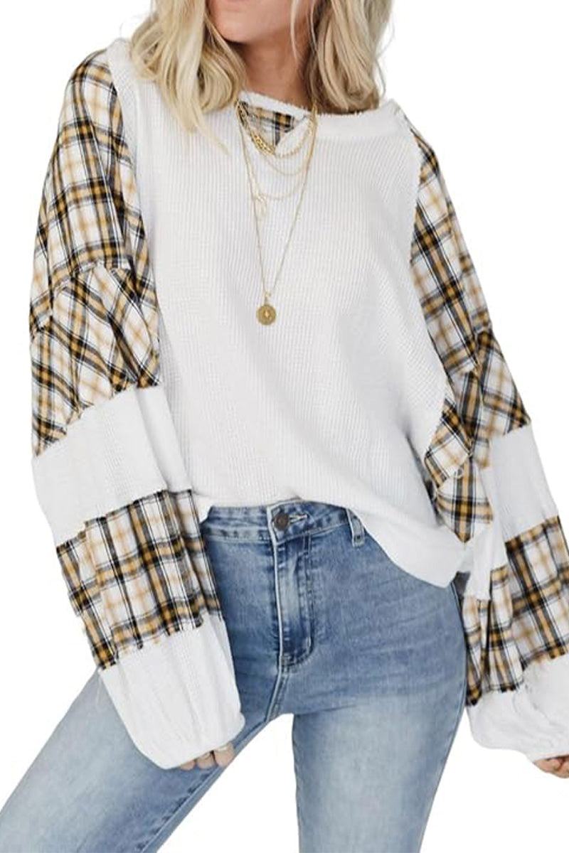 Woman wearing white waffle knit sweatshirt with plaid sleeves and gold necklaces paired with blue jeans