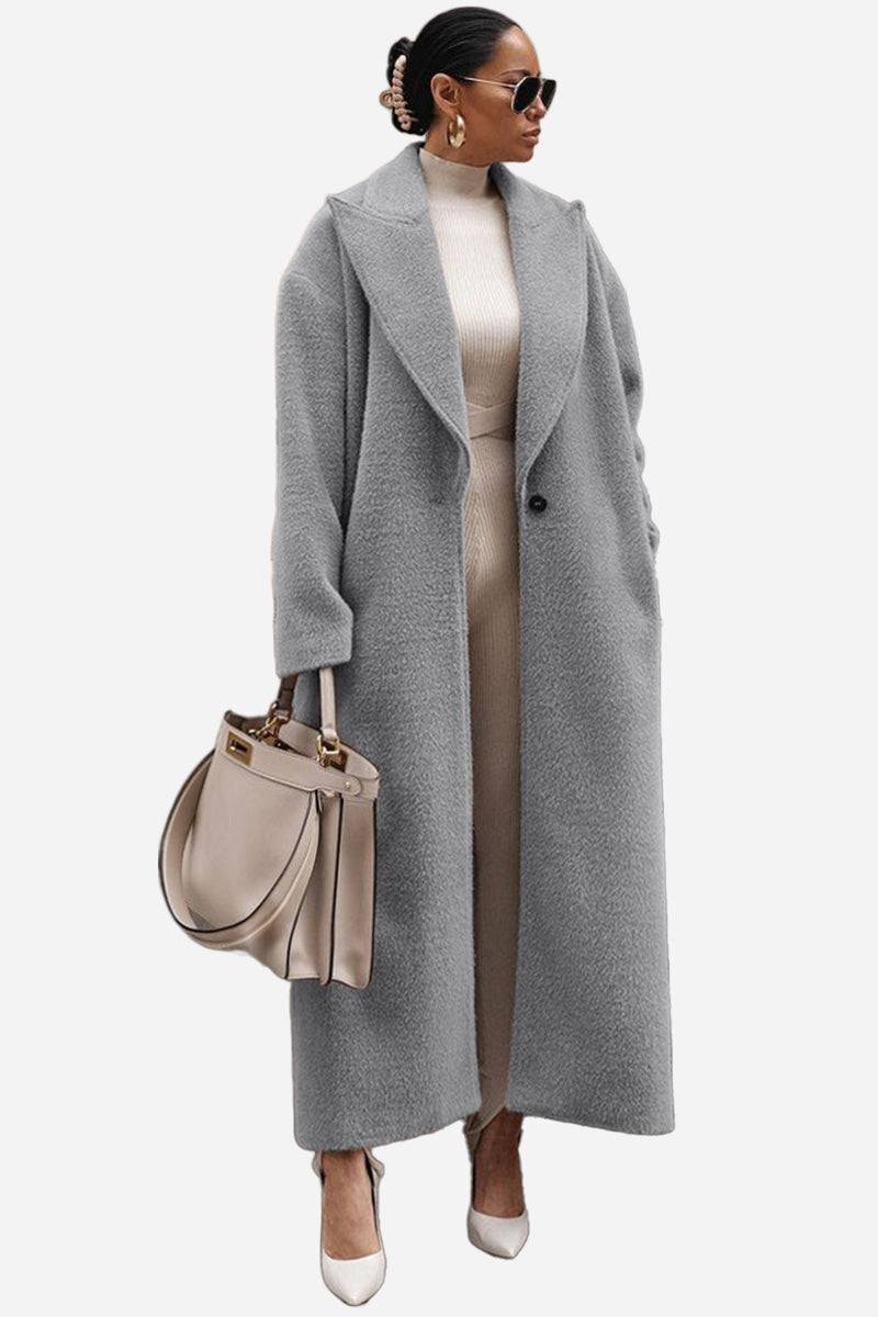 Woman wearing long grey oversized teddy coat with oversized lapels and beige outfit carrying beige handbag