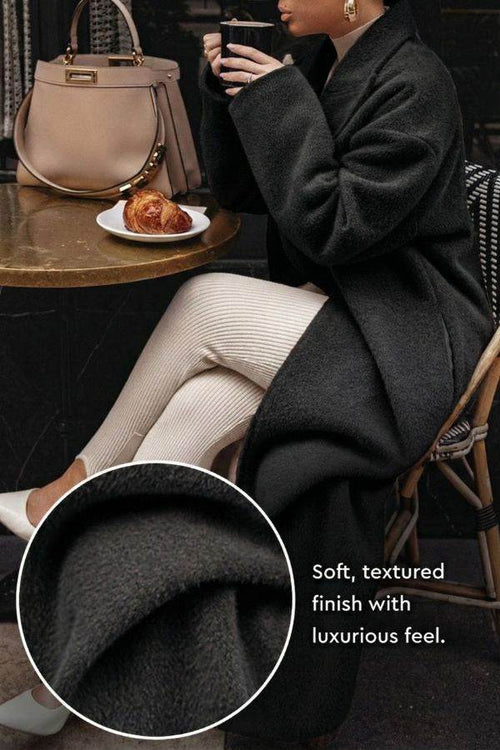 Black oversized teddy coat with soft textured fabric and relaxed fit worn by a seated woman at a café table.