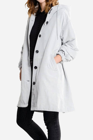 Woman wearing light grey water-resistant oversized windbreaker with hood and buttons