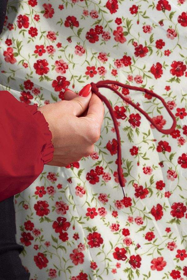Close-up of hand adjusting drawstring on red water resistant oversized windbreaker jacket with floral background
