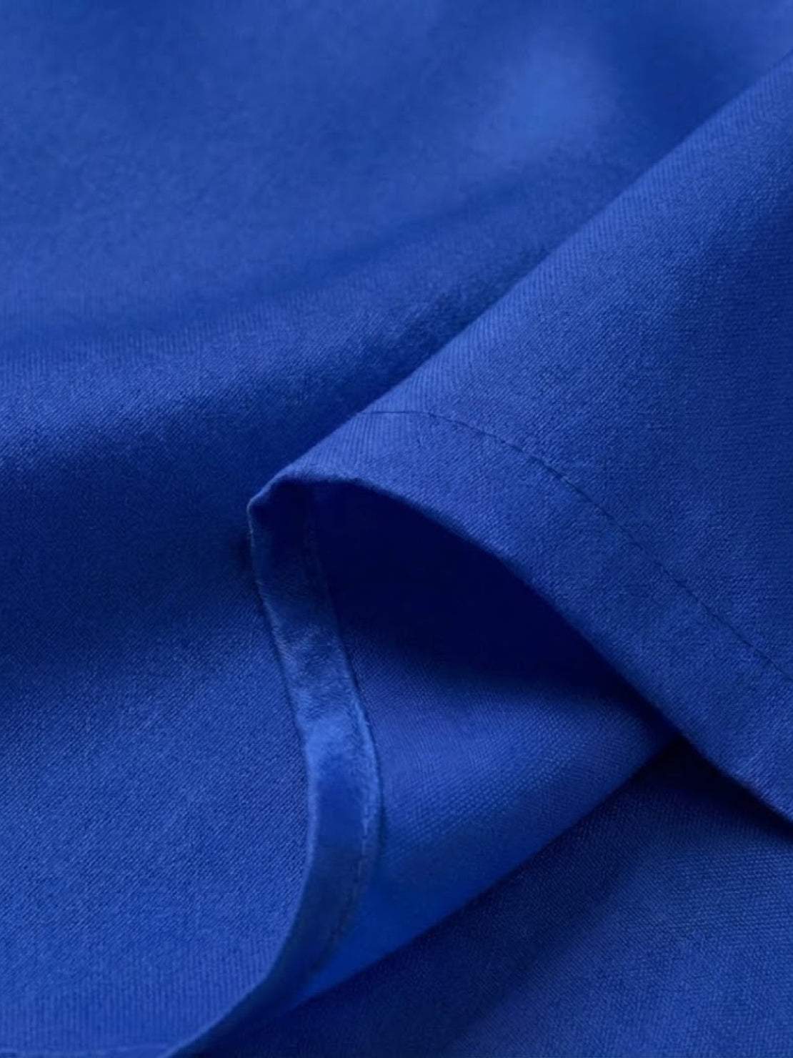 Close-up of royal blue fabric from asymmetrical two-piece trouser set with smooth, silky texture