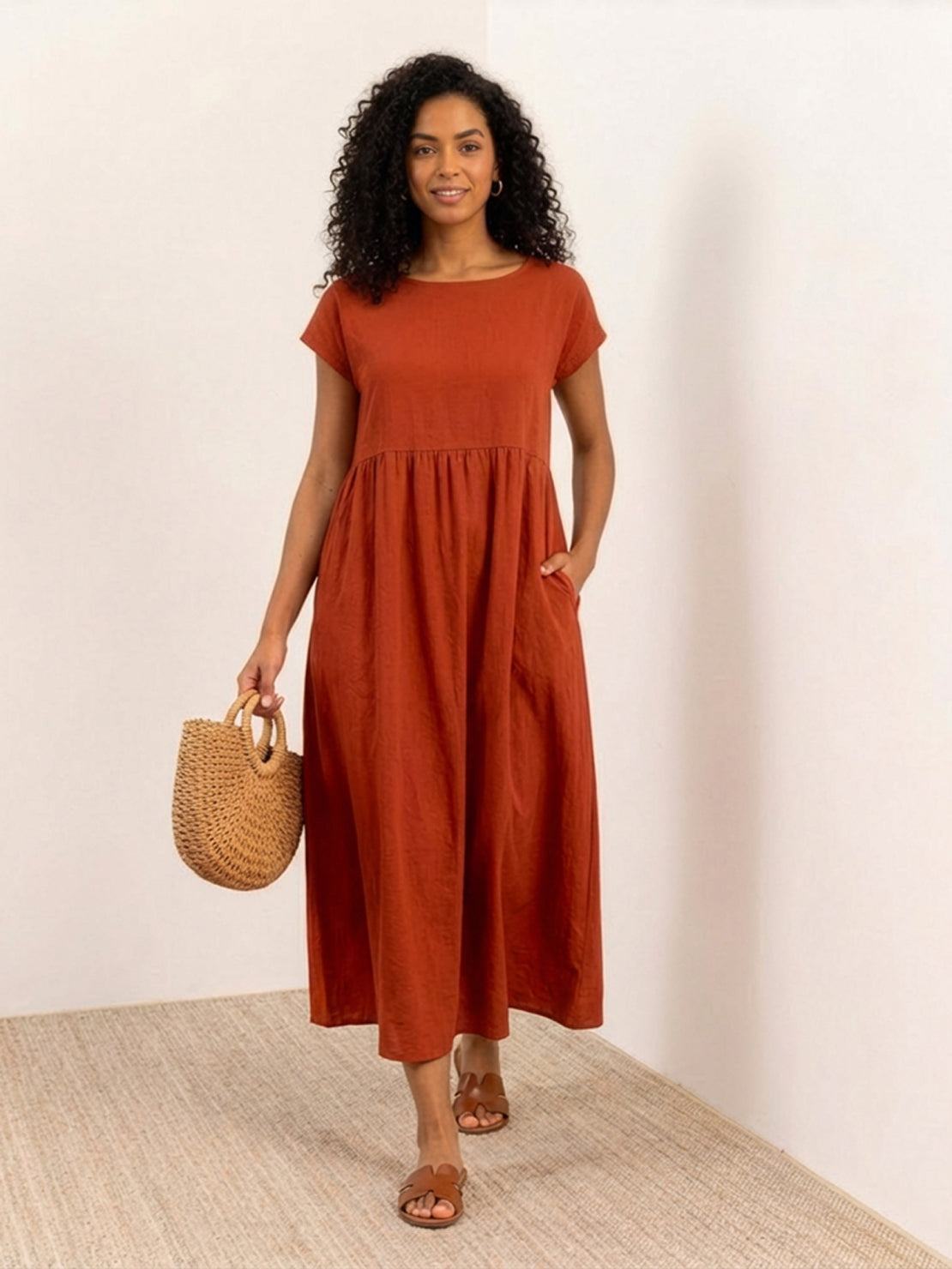 Woman wearing a capped-sleeve voluminous pleated midi dress with a flowing skirt and loose sleeves, showcasing elegance and pockets.