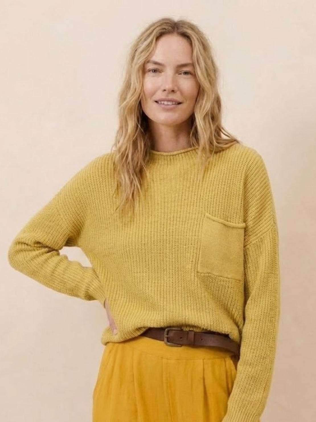 Woman wearing a mustard yellow relaxed knit sweater with a chest pocket and mustard yellow trousers, styled in European minimalism fashion
