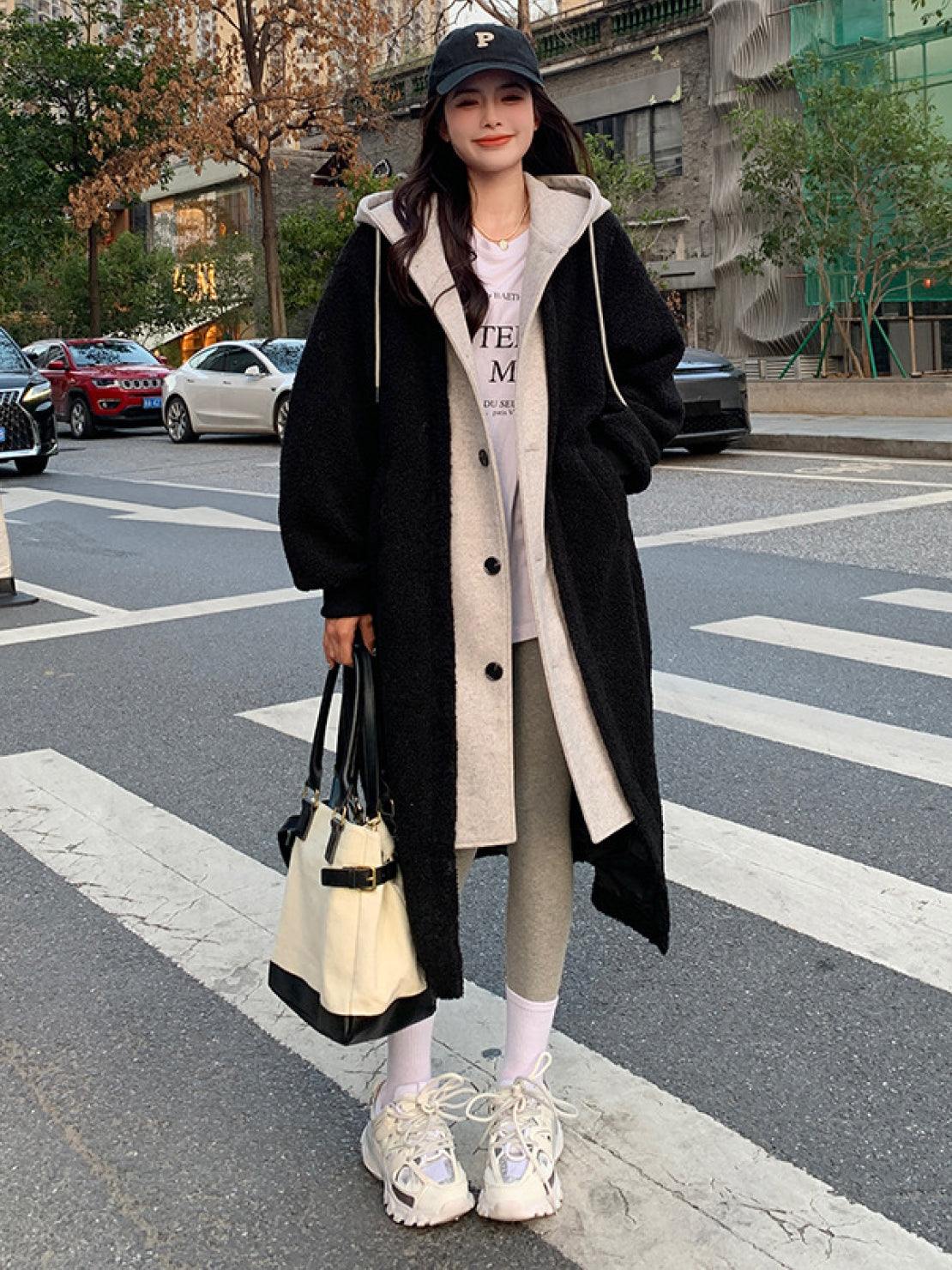 Woman wearing black oversized sherpa long coat with beige inner lining walking on city street carrying tote bag