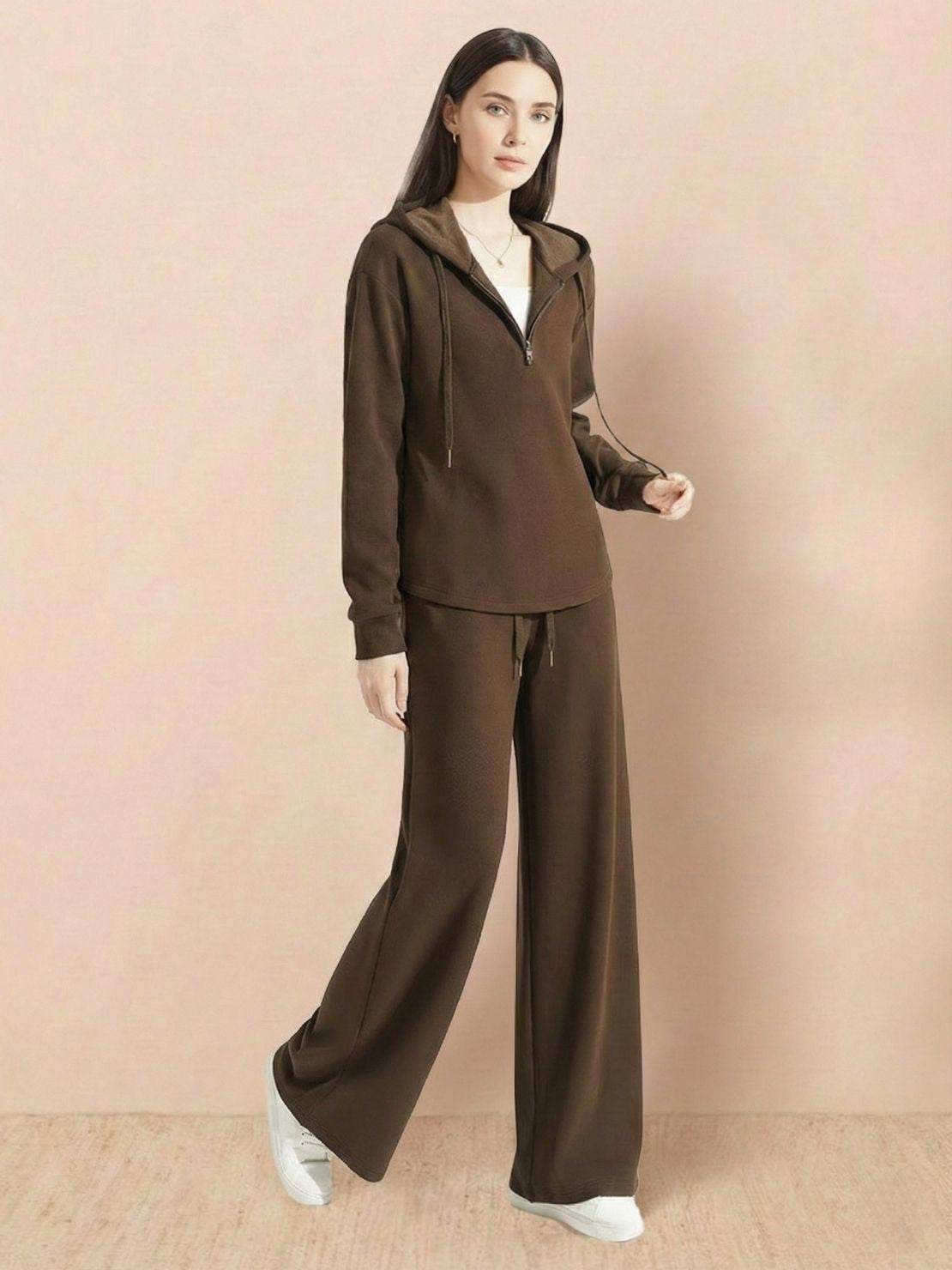 Woman wearing brown lyocell-blend hooded set with wide-leg pants and white sneakers against beige background
