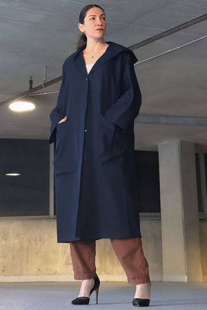 Woman wearing oversized navy water resistant windbreaker jacket with hood and front pockets standing indoors