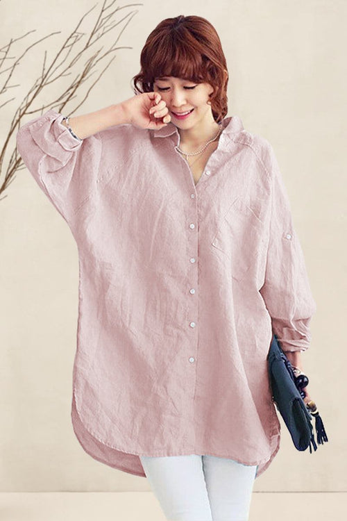 Woman wearing oversized pink linen shirt with loose sleeves and button-down front, styled casually with white pants and holding a clutch bag