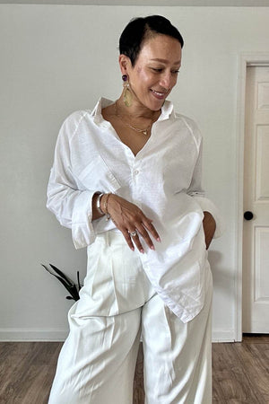 Woman wearing white oversized linen shirt with relaxed fit and white trousers indoors