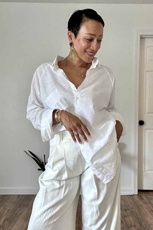 Woman wearing white oversized linen shirt with relaxed fit and white trousers indoors