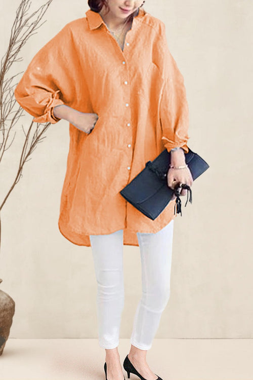 Woman wearing oversized orange linen shirt with white pants and black heels holding a black clutch bag