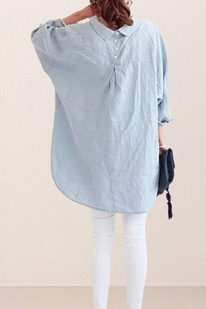 Back view of oversized linen shirt in light blue with loose sleeves and gathered back detail worn over white pants