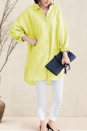 Woman wearing oversized linen shirt in light yellow with white pants and black heels holding a black clutch purse