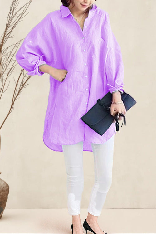 Woman wearing a pastel purple oversized linen shirt with relaxed fit, paired with white pants and black heels, holding a black clutch.