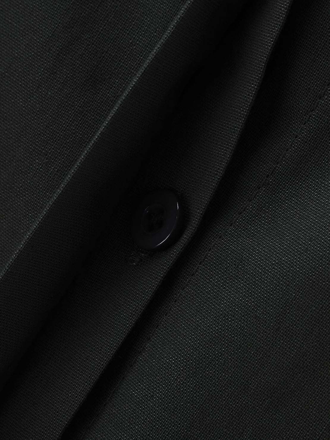 Close-up of oversized 100% cotton black shirt fabric with button detail