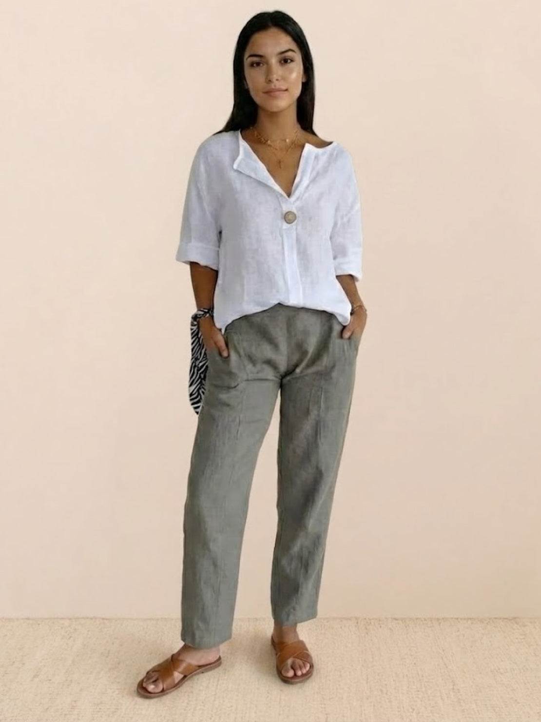 woman wearing white pure linen age-defying shirt with button detail and gray pants standing against beige background