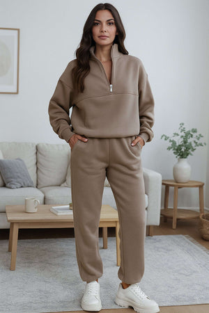 Woman wearing neutral toned cotton blend tracksuit with zip neckline and stretch waistband in a modern living room