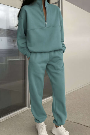 Woman wearing mint green cotton blend tracksuit with zip neckline and white sneakers, standing indoors.