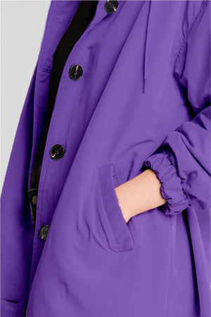 Close-up of a woman wearing a purple Rain Couture Windbreaker with oversized fit, showing buttoned front and side pocket.