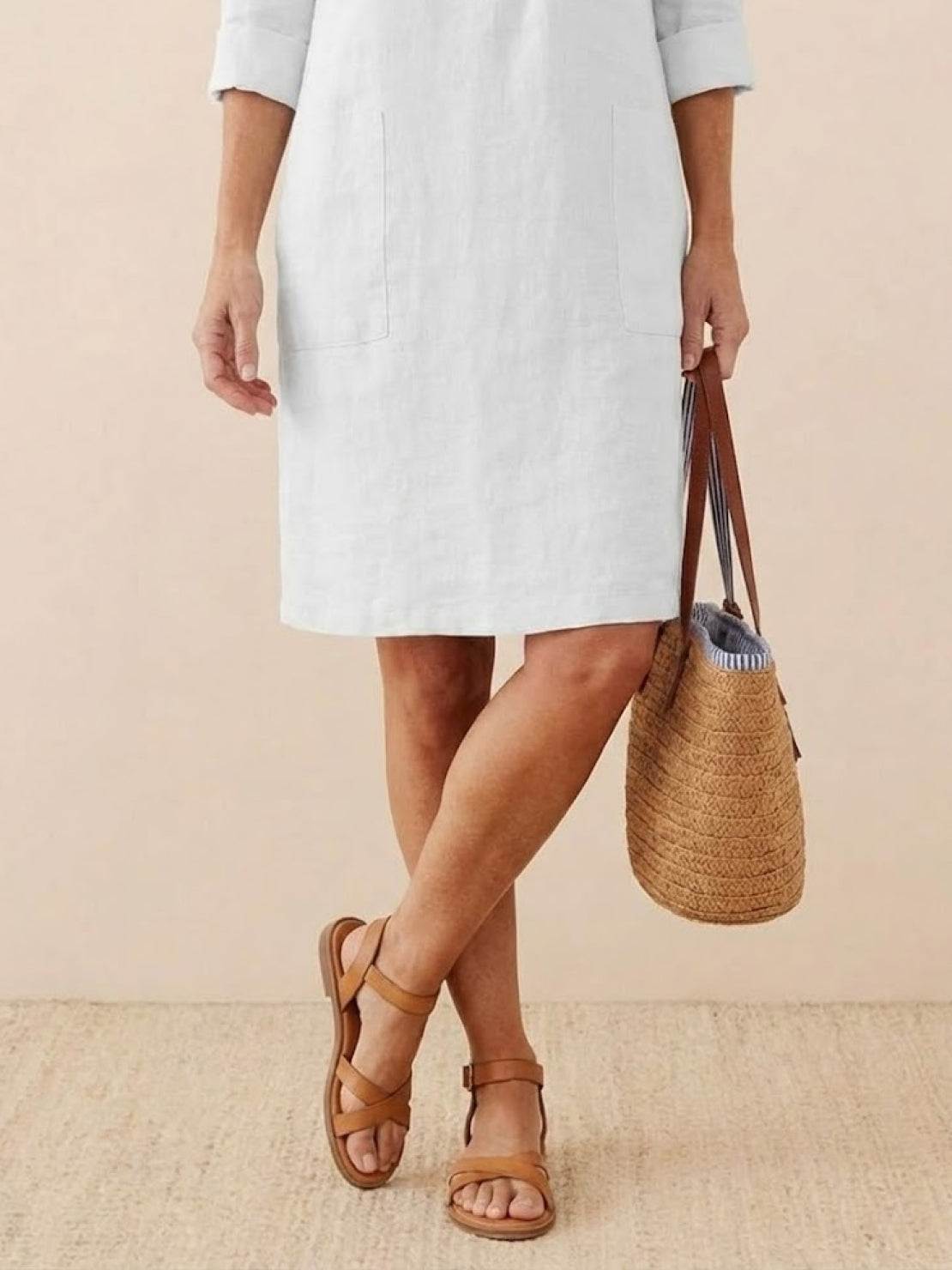 woman wearing knee-length white cotton dress with 3/4 sleeves holding woven straw bag and brown sandals