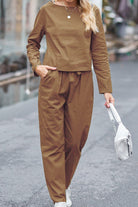 Woman wearing brown 100% cotton linen two-piece set with long sleeves and pants, holding a white handbag.